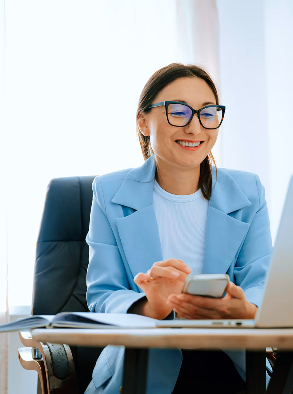 Photo d'une femme souriante à lunettes, en veste bleue, consultant son téléphone